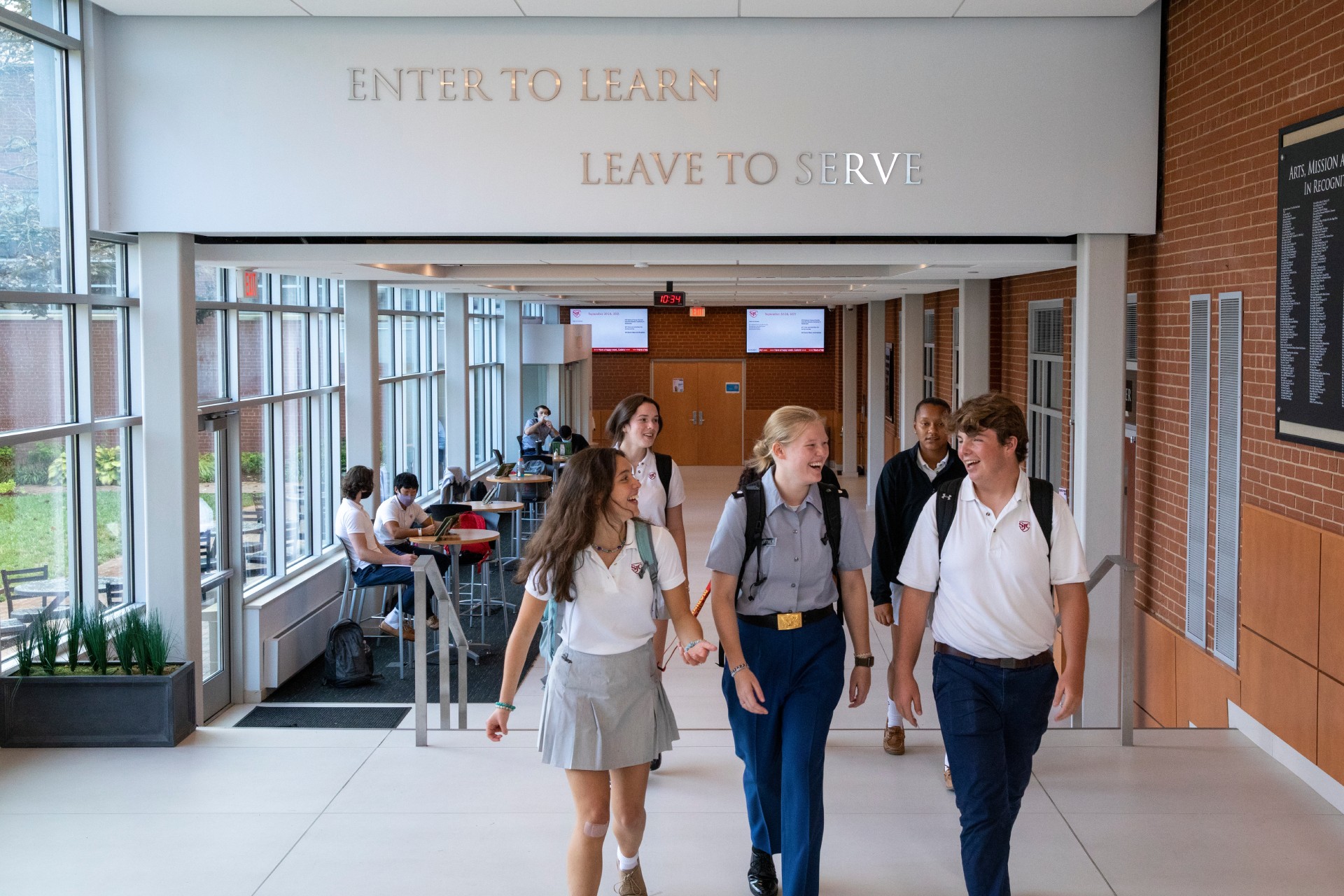 Students indoors, white wall with silver lettered quote:Enter to Learn, Leave to Serve